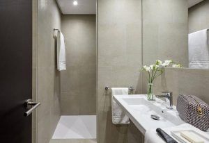 Este baño minimalista, que refleja el estilo elegante del Hotel Posada del Lucero Sevilla, incluye azulejos beige, un lavabo blanco, un toallero, un jarrón de flores y un bolso estampado en el mostrador. - ForTwo - Planes para parejas