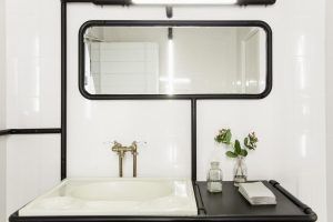 El baño minimalista del Hotel 7 Islas Madrid luce un lavabo blanco, un espejo grande y un grifo vintage con pequeñas plantas en un jarrón de cristal, creando un oasis de serenidad. - ForTwo - Planes para parejas