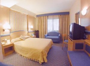 Disfrute de un remanso de paz en el Hotel Gran Versalles Madrid con una cómoda cama, televisor, sillón y escritorio. Las elegantes cortinas cubren la ventana, complementando la relajante decoración en azul y beige. - ForTwo - Planes para parejas