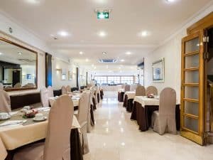 El Hotel Gran Versalles Madrid cuenta con un elegante interior con mesas cuidadosamente dispuestas, decoración en tonos beige y marrón, grandes espejos y una iluminación suave en su restaurante. - ForTwo - Planes para parejas