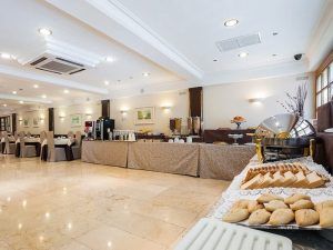 Disfrute del amplio comedor del Hotel Gran Versalles Madrid, con mesas de buffet repletas de repostería y bebidas. La elegante decoración y la suave iluminación crean un ambiente cálido y acogedor. - ForTwo - Planes para parejas