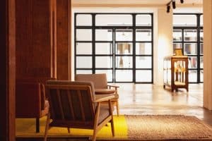 Una acogedora habitación del Hotel 7 Islas Madrid, con dos sillas, una alfombra amarilla, un armario y grandes ventanales con motivos cuadriculados al fondo. - ForTwo - Planes para parejas