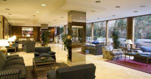 El elegante vestíbulo del Hotel Gran Versalles Madrid es acogedor, con cómodos asientos, grandes ventanales, exuberante vegetación y una iluminación cálida. - ForTwo - Planes para parejas
