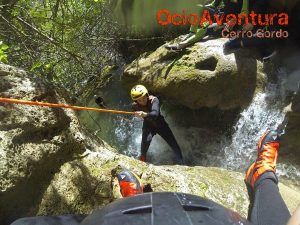 Una persona desciende hábilmente en rápel por una cascada rocosa en Jorox, usando equipo de protección. El texto superior dice "Barranquismo en Jorox de la mano de Ocio Aventura (Málaga)", capturando la emocionante esencia del barranquismo. - ForTwo - Planes para parejas