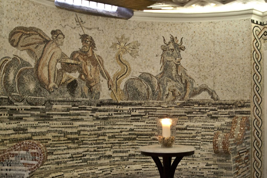 Un antiguo mosaico de figuras mitológicas del mar adorna las Termas de Hispalis, donde una mesa a la luz de las velas crea un ambiente similar a la relajante experiencia que ofrece el Circuito Termal con Masaje en las Termas de Hispalis (Sevilla). - ForTwo - Planes para parejas