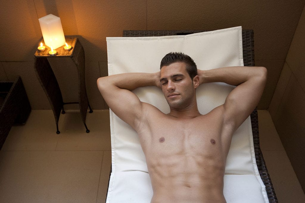 Un hombre se relaja en un sillón con los ojos cerrados, rodeado de velas en el entorno sereno del Kumaras Spa, disfrutando del rejuvenecedor Circuito spa con Masaje e infusión o zumo (Umbrete). - ForTwo - Planes para parejas