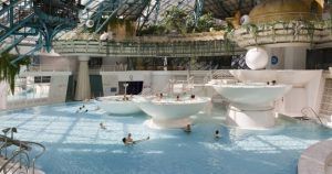 La Entrada al spa de Caldea en Andorra ofrece una piscina cubierta con plataformas circulares, un impresionante techo de cristal, exuberantes plantas y un ambiente tranquilo para el disfrute de los huéspedes. - ForTwo - Planes para parejas