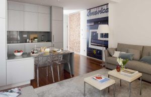 Descubra el encanto moderno de Eric Vökel Boutique Apartments con una sala de estar y una cocina de planta abierta con gabinetes grises, sillas transparentes, un cómodo sofá y un llamativo mural de tren. - ForTwo - Planes para parejas