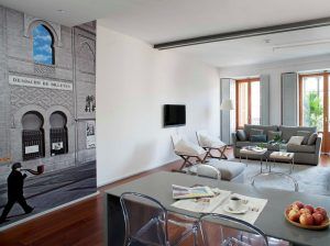 En un entorno similar a Eric Vökel Boutique Apartments, esta moderna sala de estar exhibe elegantes muebles grises, arte de pared llamativo, una elegante mesa de vidrio y un tazón de manzanas frescas en el mostrador, todo iluminado por luz natural brillante. - ForTwo - Planes para parejas