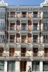 Esta maravilla arquitectónica de cinco plantas, los Apartamentos Boutique Eric Vökel, cuenta con balcones decorativos. Bajo un cielo azul despejado, dos personas pasan, personificando el encanto y la elegancia de la vida urbana. - ForTwo - Planes para parejas