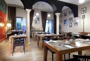 Una acogedora cafetería ubicada en el Hotel Eurostars Sevilla Boutique, con mesas de madera, sillas negras, fotografías enmarcadas en las paredes y un encantador servicio de desayuno. - ForTwo - Planes para parejas