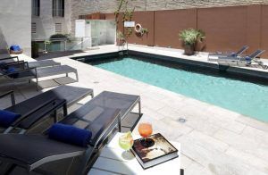 La piscina al aire libre del Hotel Eurostars Sevilla Boutique es un escape tranquilo, con tumbonas y una mesa auxiliar para bebidas y toallas, rodeada de una pared marrón y exuberante vegetación en Sevilla. - ForTwo - Planes para parejas