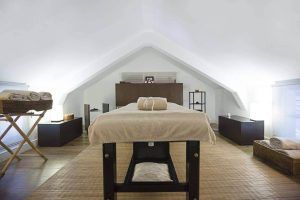 La sala de spa minimalista del Hotel Hospes Las Casas del Rey de Baeza en Sevilla ofrece una escapada tranquila con una mesa de masajes, toallas cuidadosamente dobladas y una iluminación suave bajo un techo inclinado con encanto. - ForTwo - Planes para parejas