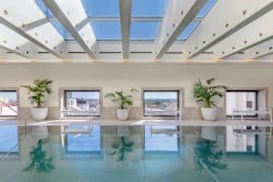 En el Hotel Barceló Torre de Madrid, esta piscina cubierta cuenta con un impresionante techo de cristal, plantas en macetas y cómodos asientos, con grandes ventanales que enmarcan bellamente el horizonte de la ciudad. - ForTwo - Planes para parejas