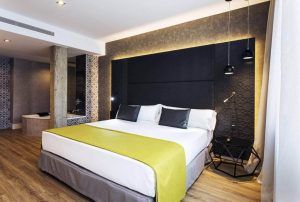 Descubra la elegancia contemporánea en el Hotel Catalonia Giralda con una iluminación elegante, una cama espaciosa, una acogedora manta amarilla y cálidos pisos de madera. - ForTwo - Planes para parejas