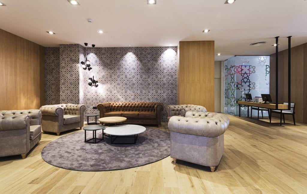 El moderno salón del Hotel Catalonia Giralda incluye cómodos sofás, una alfombra redonda, mesas de centro anidadas, suelos de madera y una decoración de paredes estampada. - ForTwo - Planes para parejas