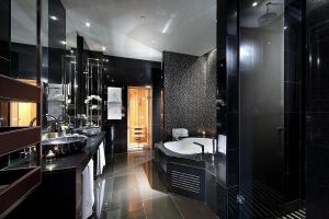 Experimente el lujo en el baño con azulejos negros del Hotel Eurostars Madrid Tower, completo con una bañera redonda, lavabos dobles e iluminación suave. - ForTwo - Planes para parejas
