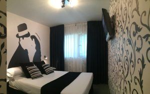 Experimente la elegancia chic de la moderna habitación de Hotel Indiana (Madrid) con una cama doble, decoración en blanco y negro, arte de pared con siluetas cautivadoras y un elegante televisor montado en la pared. - ForTwo - Planes para parejas