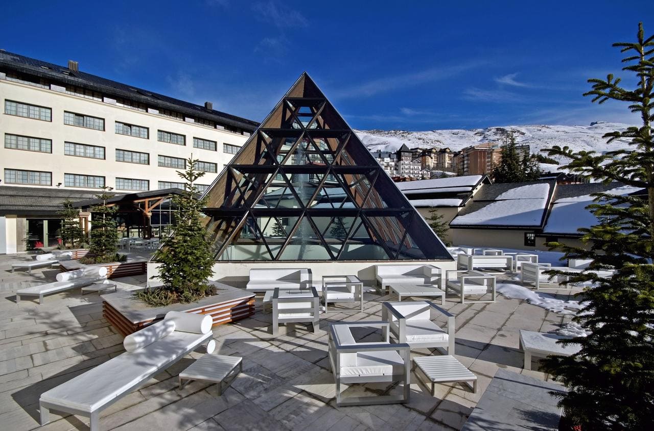 Con la Sierra Nevada como telón de fondo, este salón presume de elegantes muebles blancos y una imponente pirámide de cristal. El paisaje nevado ofrece tranquilidad, con el emblemático Hotel Meliá Sol y Nieve en Sierra Nevada (Granada) visible a lo lejos. - ForTwo - Planes para parejas