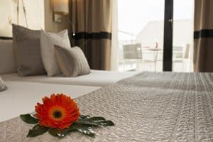 Una flor de naranja adorna la cama en una habitación moderna y suavemente iluminada del Hotel Paseo Del Arte (Madrid), con puertas abiertas que conducen al balcón y le dan la bienvenida para experimentar la vibrante atmósfera de Madrid. - ForTwo - Planes para parejas
