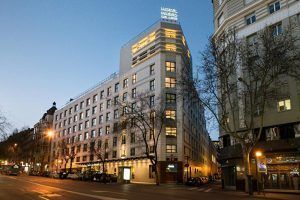 Vista de la calle del Hotel Paseo Del Arte (Madrid), de varios pisos, que muestra su señalización iluminada y cálidamente brillante al anochecer. - ForTwo - Planes para parejas