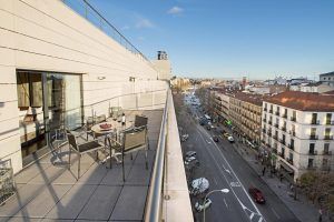 La terraza de la azotea del Hotel Paseo Del Arte (Madrid) ofrece un comedor con vistas a una calle animada, rodeada de edificios contra un cielo azul claro. - ForTwo - Planes para parejas