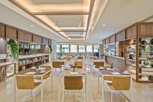 El Hotel Meliá Princesa de Madrid cuenta con un moderno restaurante con mesas y sillas de madera, elegantes luces de techo y exuberantes plantas que adornan las estanterías. - ForTwo - Planes para parejas