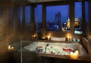 Disfrute de un baño de lujo en el Hotel Meliá Princesa de Madrid, donde las velas y los pétalos de rosa crean un ambiente sereno. Contemple el impresionante horizonte nocturno de la ciudad a través de sus amplios ventanales. - ForTwo - Planes para parejas