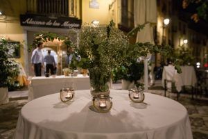 Una mesa de comedor al aire libre con vegetación y tres velas se encuentra cálidamente iluminada en la calle cerca del Restaurante Alacena de las Monjas en Granada, que ofrece su Menú Aljibe. - ForTwo - Planes para parejas