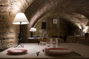 Experimente el encanto de Granada en el Restaurante Alacena de las Monjas: un acogedor sótano con arcos de ladrillo, cálida iluminación de lámparas y mesas decoradas con el exquisito Menú Aljibe. - ForTwo - Planes para parejas