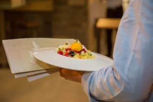 En el Restaurante Alacena de las Monjas en Granada, alguien sirve una vibrante ensalada de frutas mixtas junto con el Menú Aljibe en el Restaurante Alacena de las Monjas, brindando una deliciosa experiencia culinaria en un ambiente elegante. - ForTwo - Planes para parejas