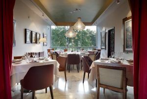 Restaurante Abades en Ronda ofrece un interior elegante con mesas dispuestas para cenar frente a grandes ventanales adornados con cortinas rojas, creando el ambiente perfecto para un "Menú romántico en el restaurante Abades (Ronda). - ForTwo - Planes para parejas