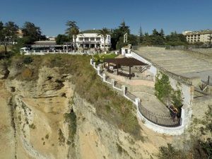 El Restaurante Abades en Ronda ofrece una experiencia gastronómica única en lo alto de un acantilado con asientos al aire libre y una pasarela vallada con vistas a un precipicio, ideal para disfrutar del Menú romántico en el Restaurante Abades bajo el cielo azul claro. - ForTwo - Planes para parejas