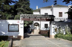 Entrada al edificio blanco con el cartel de Abades Ronda, un encantador restaurante en Ronda, es famoso por su Menú romántico en el restaurante Abades (Ronda), rodeado de árboles y vegetación. - ForTwo - Planes para parejas