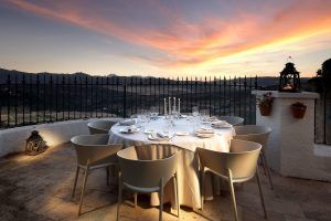 Disfrute de una velada romántica en el Restaurante Abades, donde el comedor al aire libre incluye una mesa redonda con mantel blanco y velas. Mientras el sol se pone sobre la sierra de Ronda, disfrute de cada momento con su exquisito "Menú romántico en el restaurante Abades (Ronda)". - ForTwo - Planes para parejas