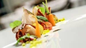 Saborea el exquisito plato del Restaurante Azahar (Sevilla), que combina carne cortada fina, tomates cherry, zanahorias, verduras frescas y una salsa amarilla vibrante en un plato blanco: una verdadera delicia culinaria. - ForTwo - Planes para parejas