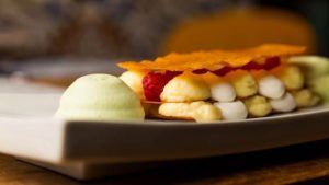 En el Restaurante Bache San Pedro de Sevilla se sirve un postre gourmet con capas de crema, frambuesas y una oblea crujiente sobre un plato blanco impecable. - ForTwo - Planes para parejas