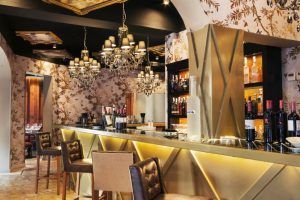 Restaurante Küche (Madrid) cuenta con lámparas de araña, un mostrador de mármol con botellas, paredes empapeladas con motivos florales y sillas alrededor de la barra para evocar la esencia vibrante de Madrid. - ForTwo - Planes para parejas