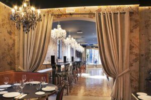 El elegante interior del Restaurante Küche (Madrid) luce lámparas de araña, cortinas decorativas y cómodos asientos, capturando el encanto de un restaurante madrileño. Las acogedoras mesas preparadas prometen a los comensales una experiencia culinaria exquisita. - ForTwo - Planes para parejas