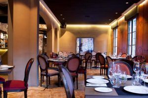 El elegante interior del Restaurante Küche en Madrid cuenta con mesas cuidadosamente dispuestas, sillas de madera, iluminación suave y obras de arte enmarcadas en la pared, creando un ambiente acogedor que captura tanto la esencia del restaurante como la cocina tradicional. - ForTwo - Planes para parejas