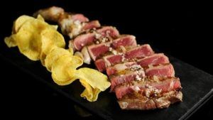Filete de ternera con escamas de sal y patatas fritas crujientes servido en un plato rectangular negro en el Restaurante L'expérience (Málaga), una delicia culinaria. - ForTwo - Planes para parejas
