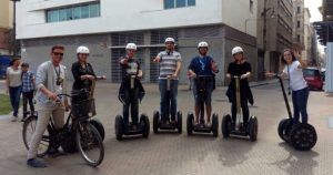 Un grupo de personas con cascos pasea alegremente en Segways y bicicletas por una calle de la ciudad, capturando la vibrante energía de Málaga mientras sonríen y posan durante su emocionante "Ruta en segway por Málaga". - ForTwo - Planes para parejas