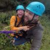 Dos personas, ataviadas con casco y riendo alegremente, se embarcan en un emocionante "Salto puenting tandem en pareja en Saldes" entre una exuberante vegetación. - ForTwo - Planes para parejas