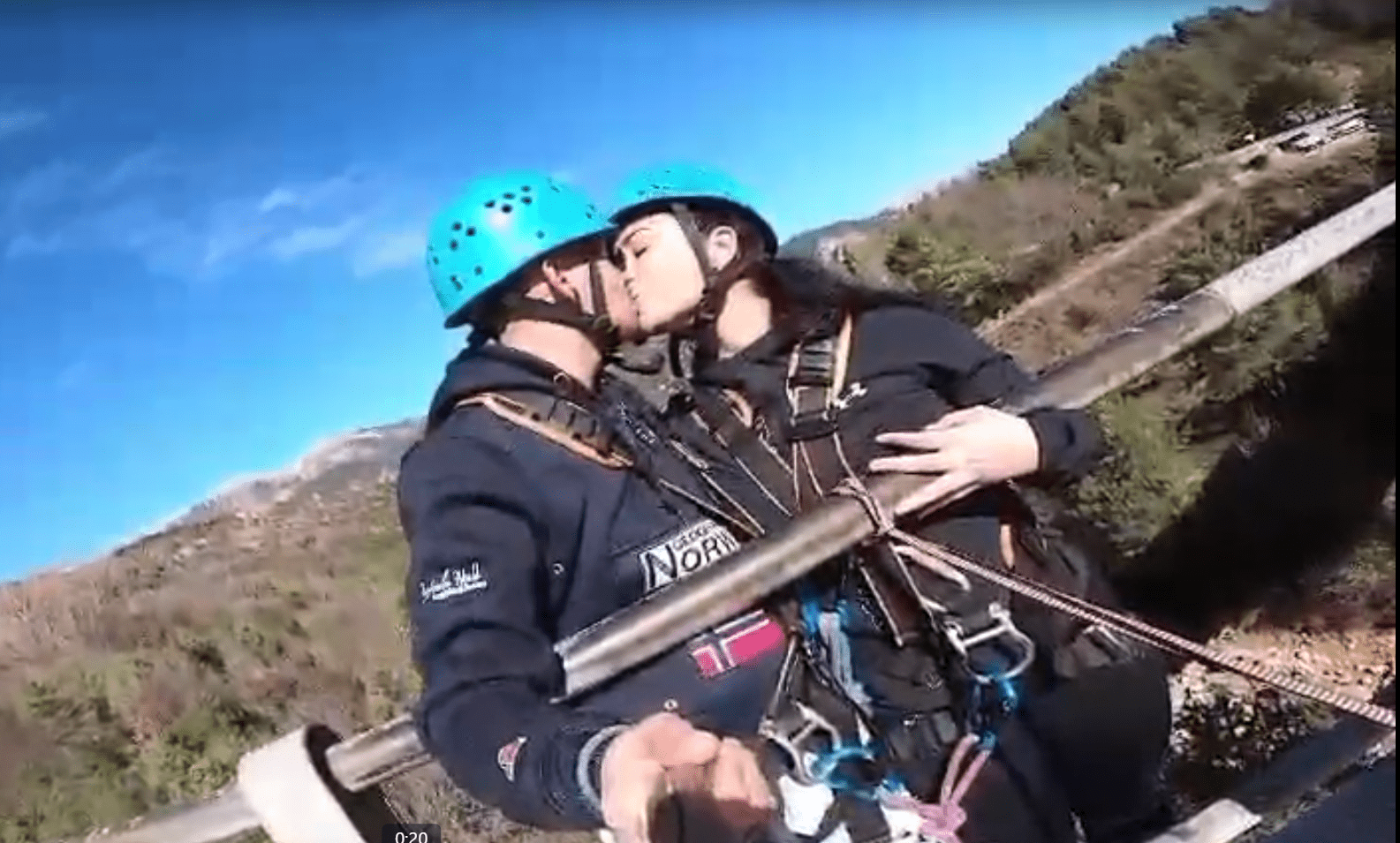 Una pareja, equipada con cascos y arneses, comparte un beso en un puente durante su emocionante aventura "Salto puenting tandem en pareja en Saldes" en medio del pintoresco paisaje. - ForTwo - Planes para parejas