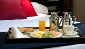En el Hotel Vincci Soho de Madrid, disfrute de una mañana acogedora con un desayuno en la cama sobre vibrantes almohadas rojas. Deléitese con fruta fresca, bollería caliente, zumo de naranja y café caliente servido en elegantes cafeteras de plata. - ForTwo - Planes para parejas