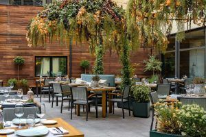 El patio exterior del Hotel Vincci Soho (Madrid) está elegantemente diseñado con paredes de madera, mesas de comedor y una exuberante vegetación que lo cubre. - ForTwo - Planes para parejas