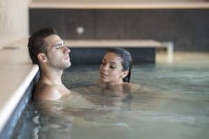 Un hombre y una mujer se relajan en una piscina cubierta del Kumaras Spa, como parte de la experiencia de 90 minutos del Circuito Termal. El hombre se apoya cómodamente en el borde. - ForTwo - Planes para parejas
