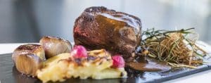 Un filete de ternera al plato con salsa rica, ajo asado, verduras a la parrilla y guarnición de hierbas sobre una pizarra crea el escenario perfecto para una cena romántica de lujo en el Restaurante Abades Triana (Sevilla). - ForTwo - Planes para parejas