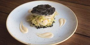 En el Restaurante Dos Cielos de Madrid, saboree un plato gourmet con suculentas gambas, crujiente escarola, rica trufa negra en un plato blanco y una cremosa salsa de acompañamiento. Disfrute de una cena exquisita en el vibrante corazón de la escena culinaria de la ciudad. - ForTwo - Planes para parejas