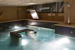 El Circuito Termal del Kumaras Spa (Umbrete) cuenta con una piscina cubierta con elementos de agua iluminados y una suave cascada que ofrece una experiencia serena en medio de paredes elegantemente revestidas. - ForTwo - Planes para parejas
